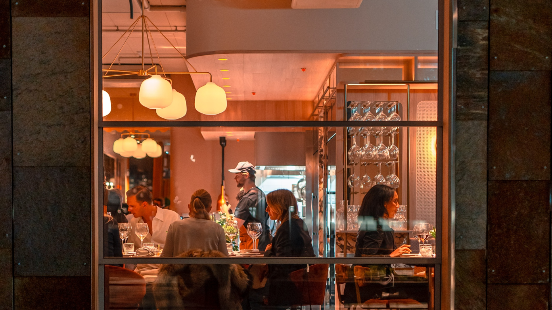 Gjester i en restaurant i Bjørvika sett gjennom vinduet om kvelden